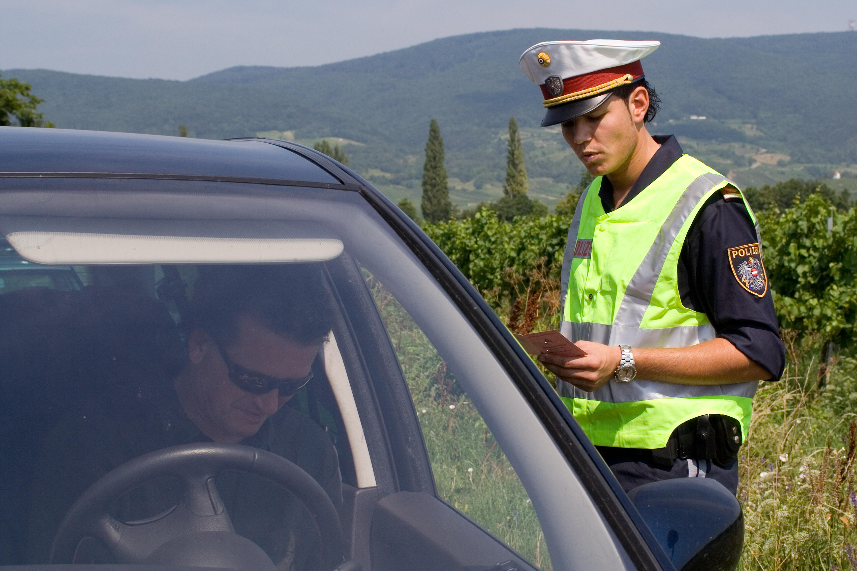 Eine Exekutivbedienstete im Polizeidienst prüft bei einer Fahrzeugkontrolle die Papiere des angehaltenen Fahrers.