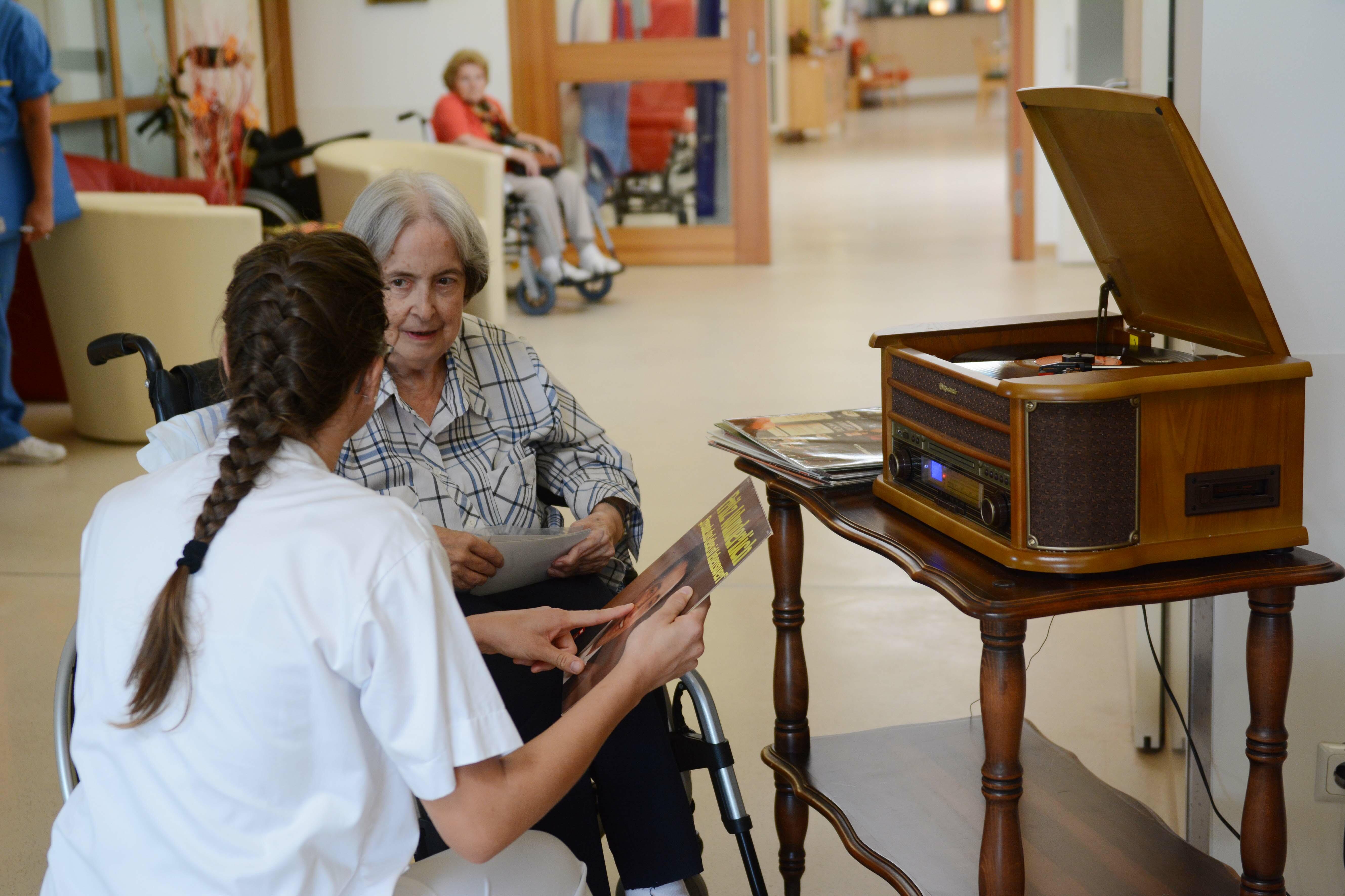 Eine Pflegerin sucht mit einer älteren Frau gemeinsam eine Schallplatte aus.
