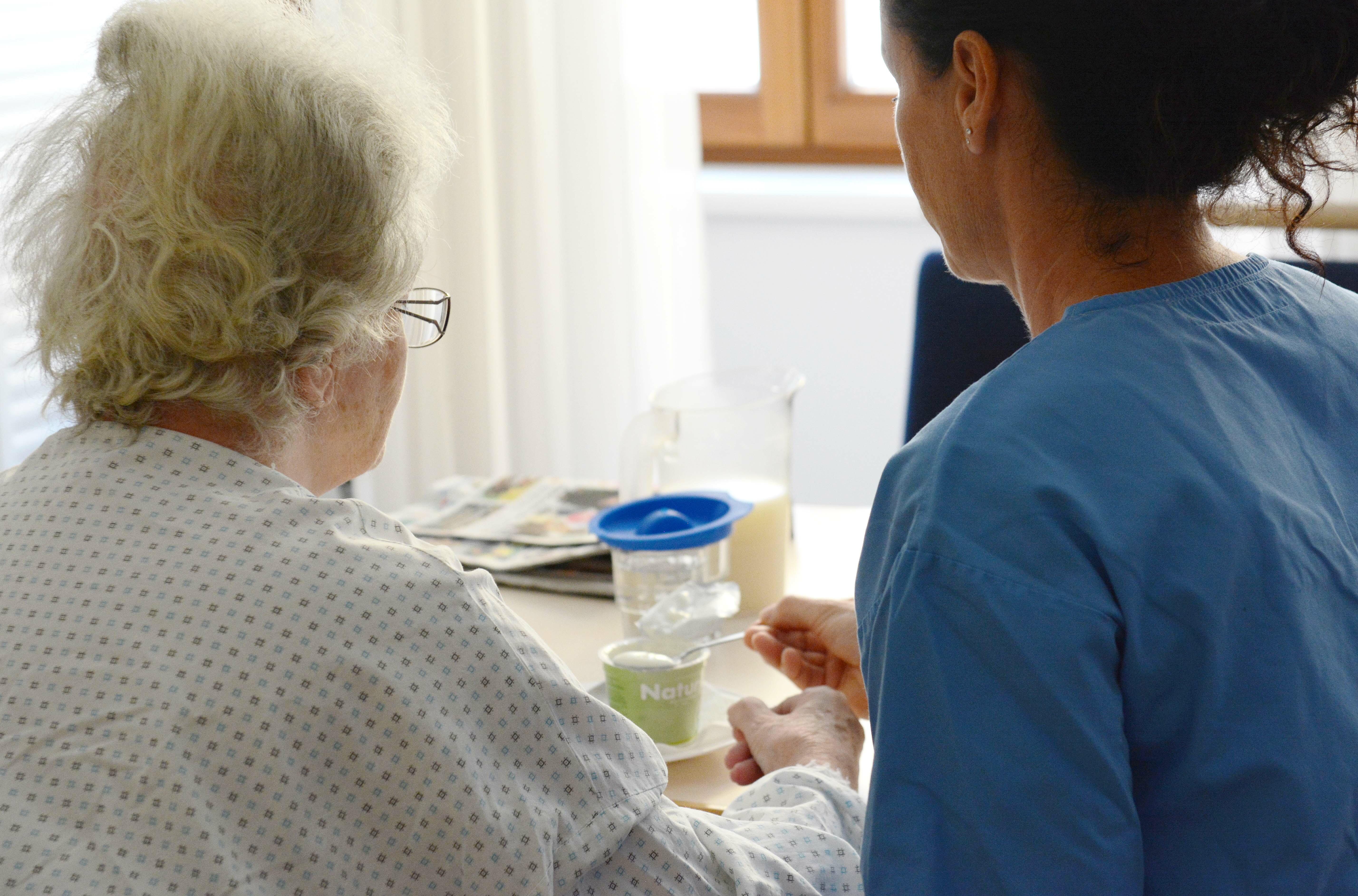 Eine Pflegekraft unterstützt eine ältere Dame beim Essen.