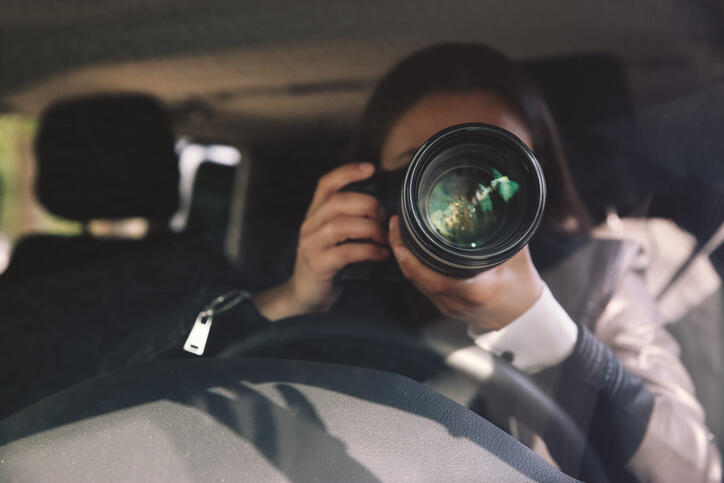Eine Detektivin fotografiert vom Auto aus mit einer professionellen Kamera.