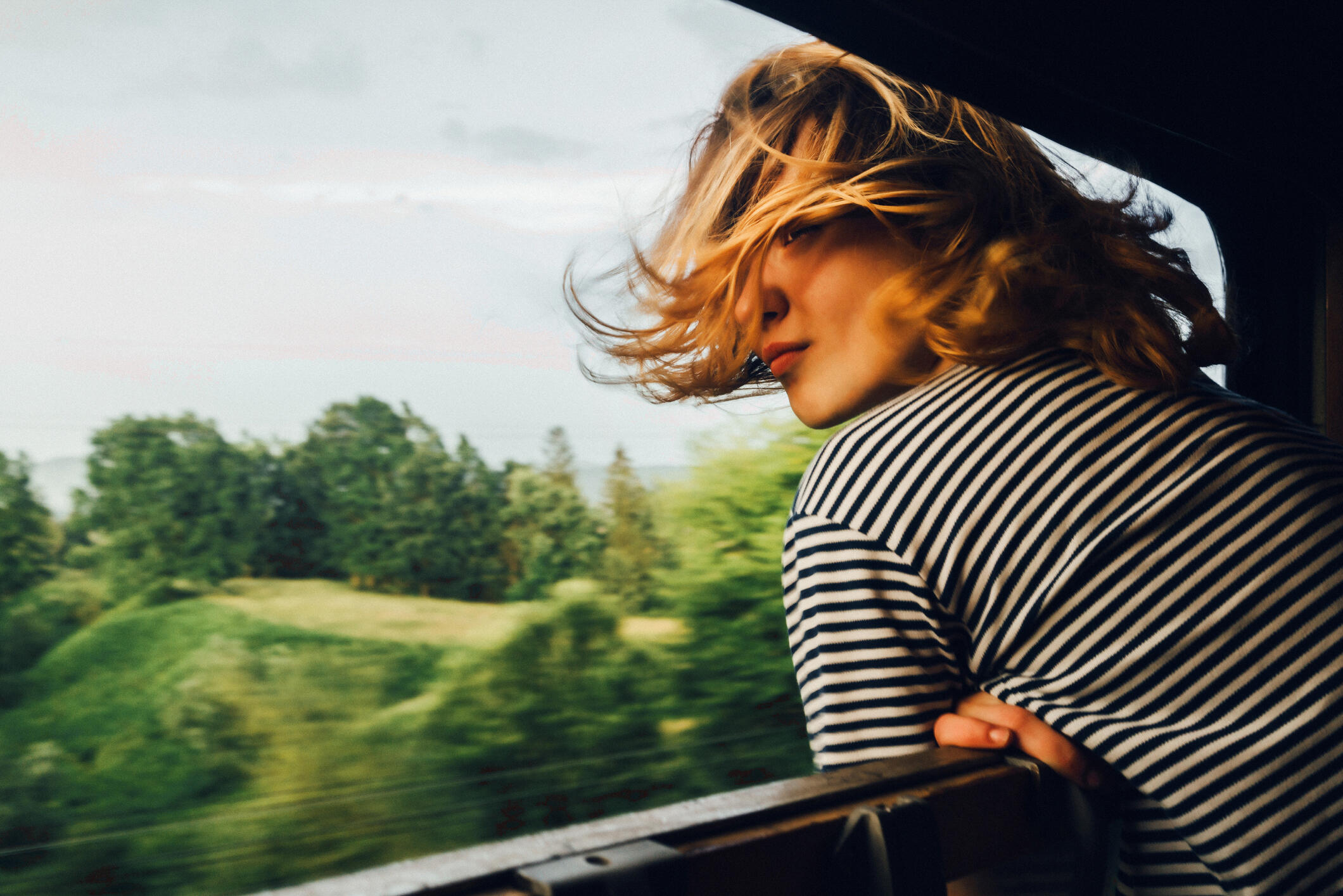 Eine junge Frau lehnt sich aus dem Fenster eines fahrenden Zuges und blickt in die Landschaft.